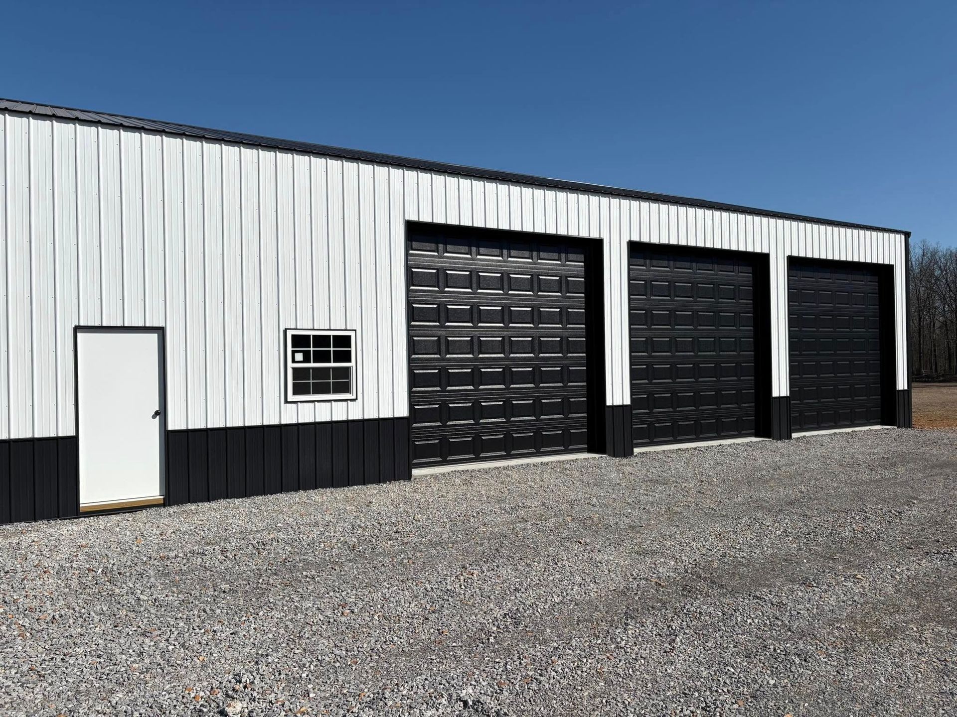 Exterior of a white and black metal building with three black garage doors, a small window, and a white door.