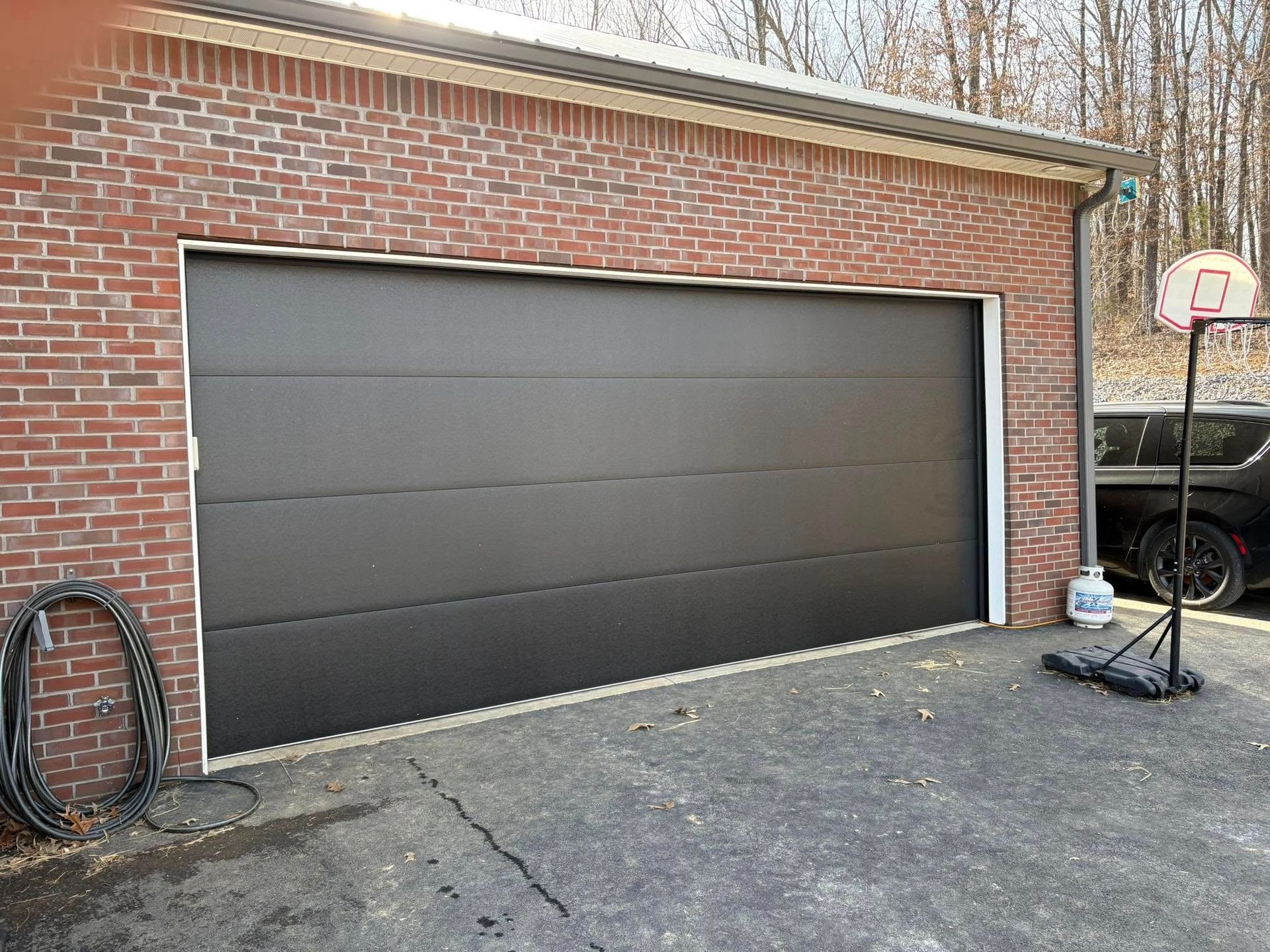 Black garage door on a brick building, with a basketball hoop and a car in the background.