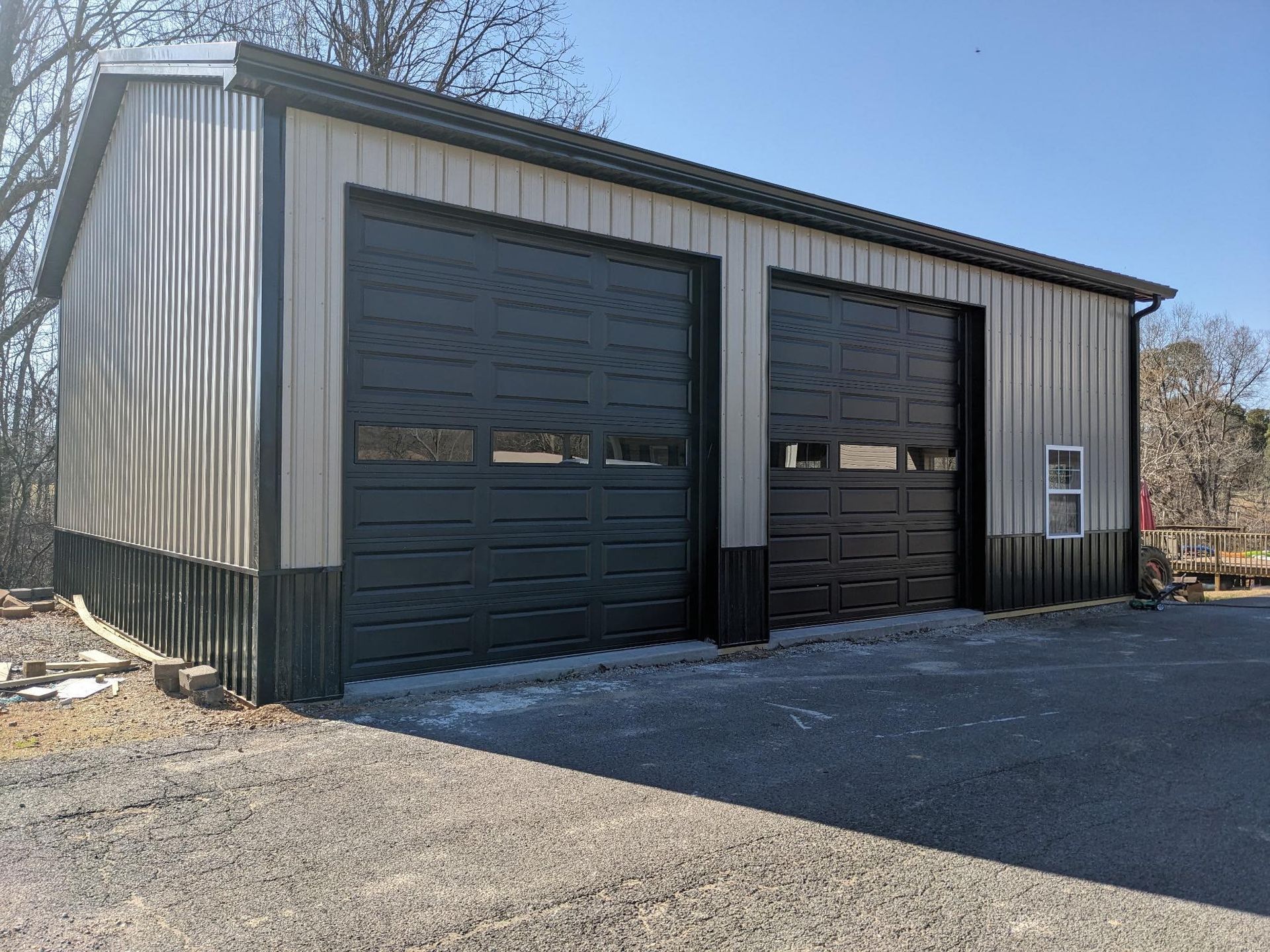 Metal garage with two black garage doors, gravel driveway, and a clear sky.