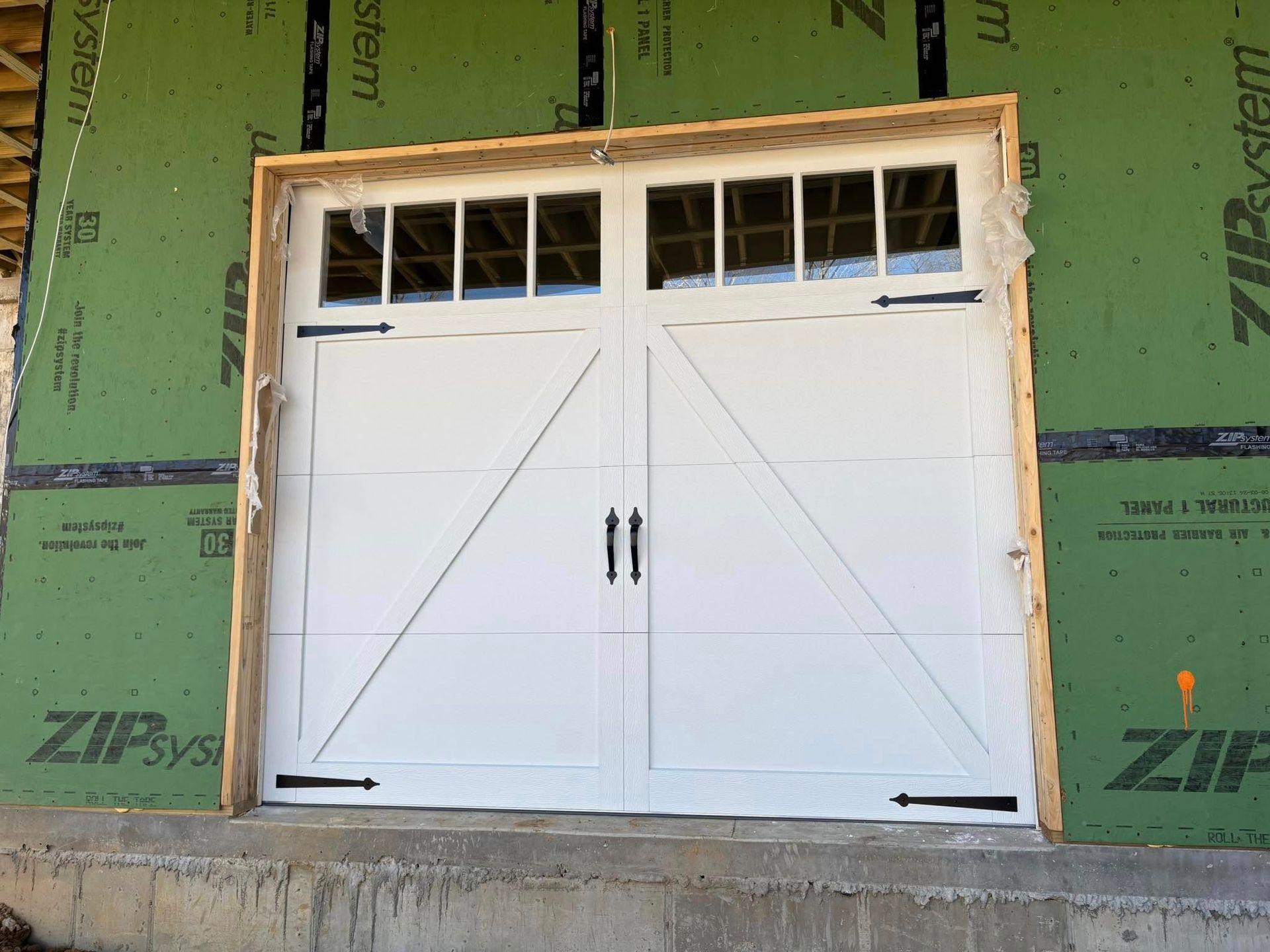 White double garage door with glass panes, black hardware, and diagonal accents, set in a wooden frame.
