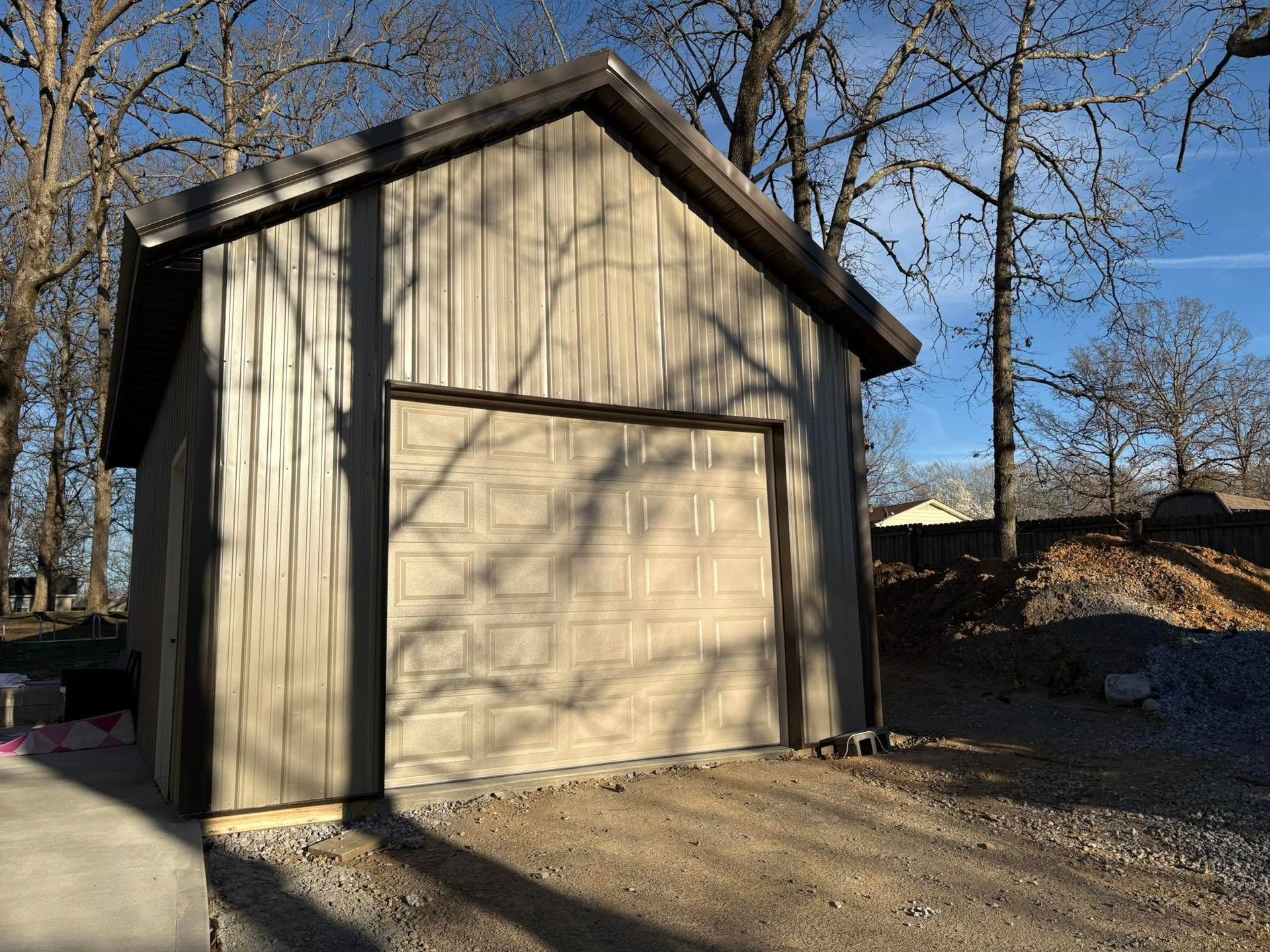 Tan garage with brown trim and a closed garage door, outdoors with trees.