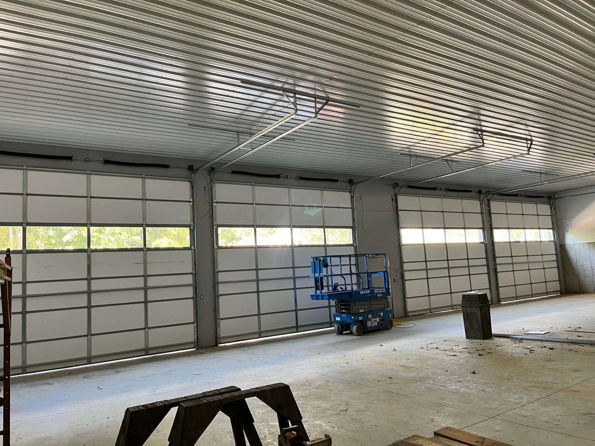 Interior view of a building with several large garage doors, metal ceiling, and a lift.