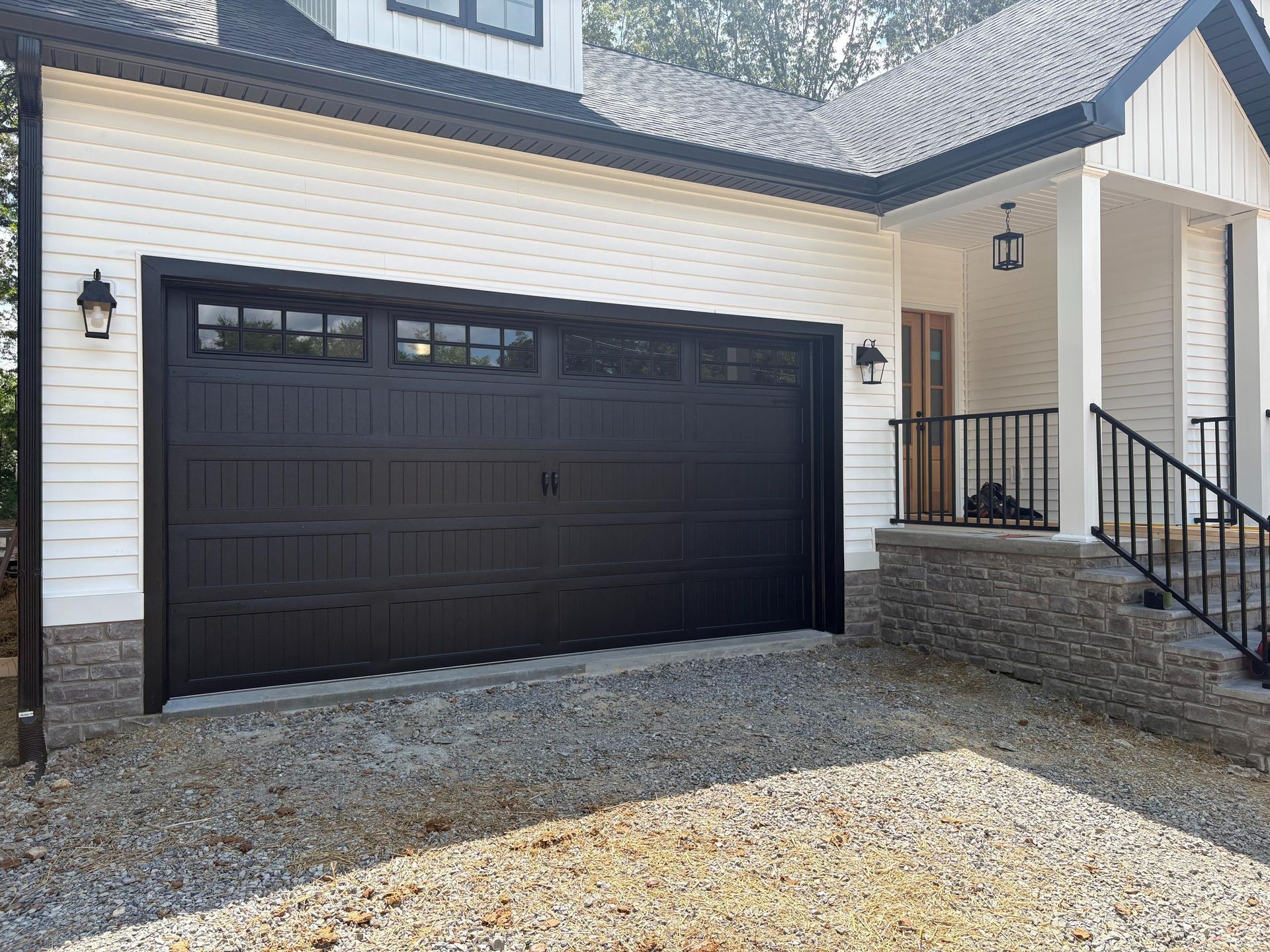 Black garage door on a white house with black trim, gravel driveway, and black lights.