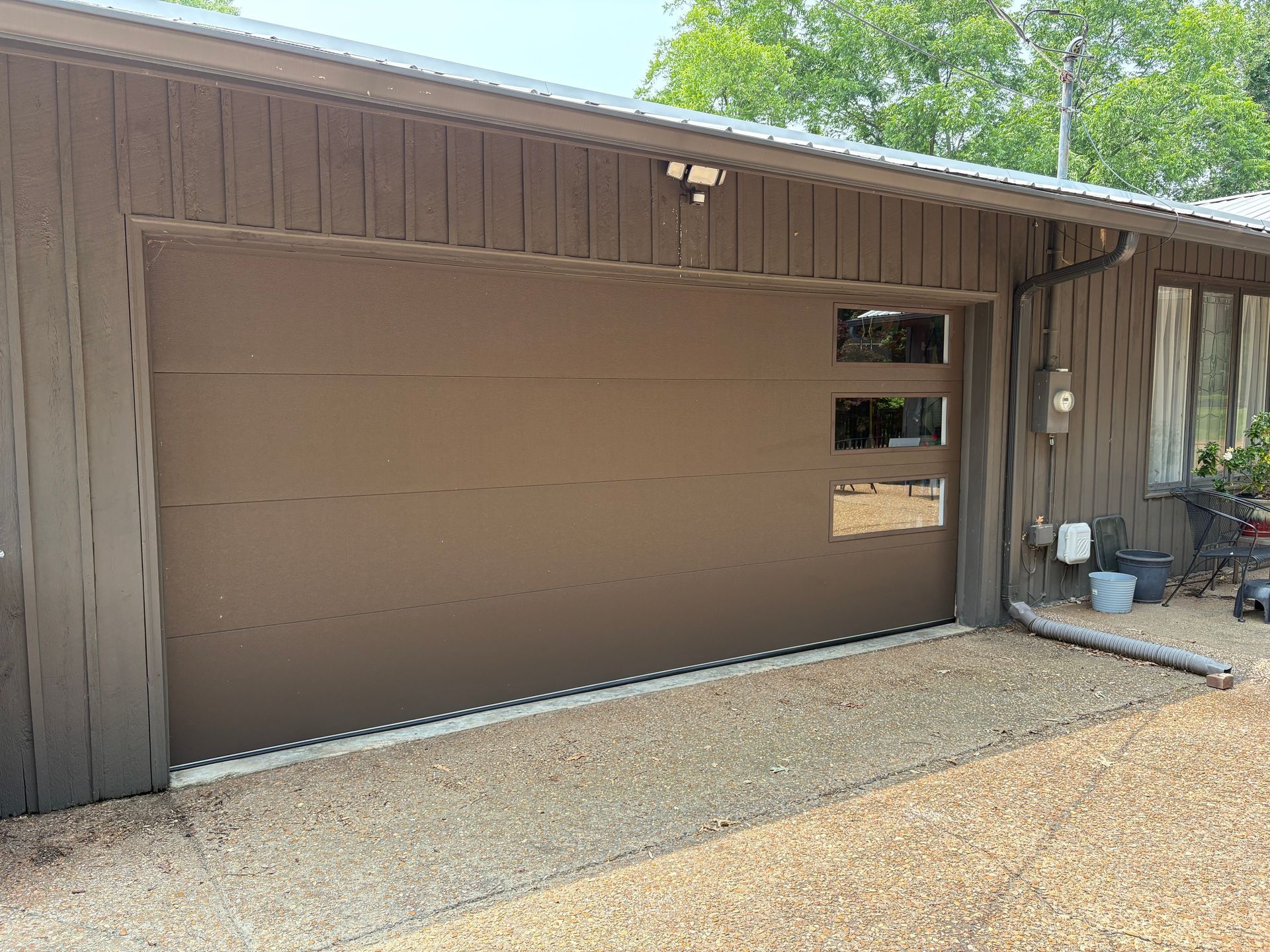 Brown garage door with three square windows, gravel driveway.