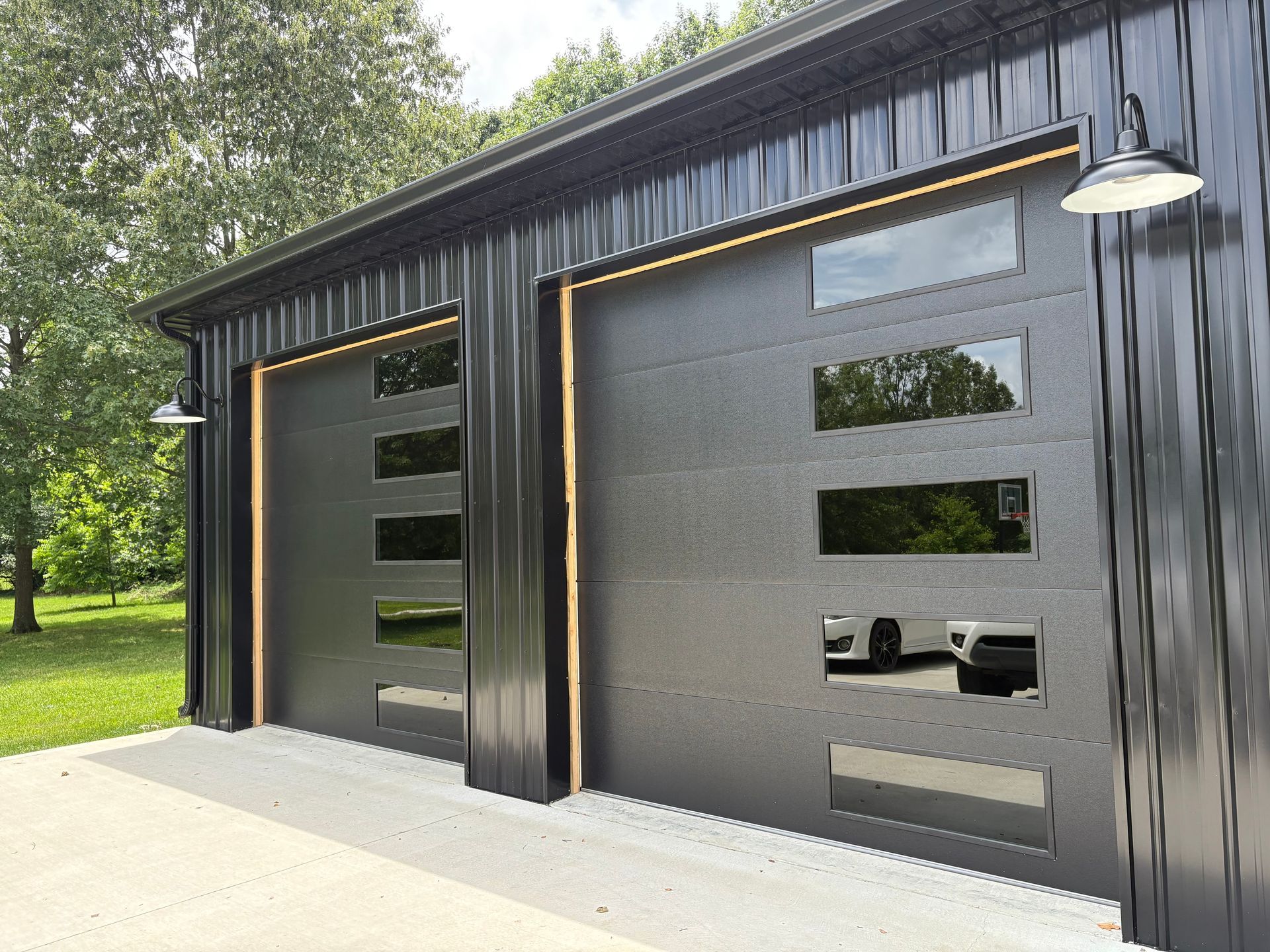 Black metal garage doors with windows, outlined in gold, and outdoor lights.