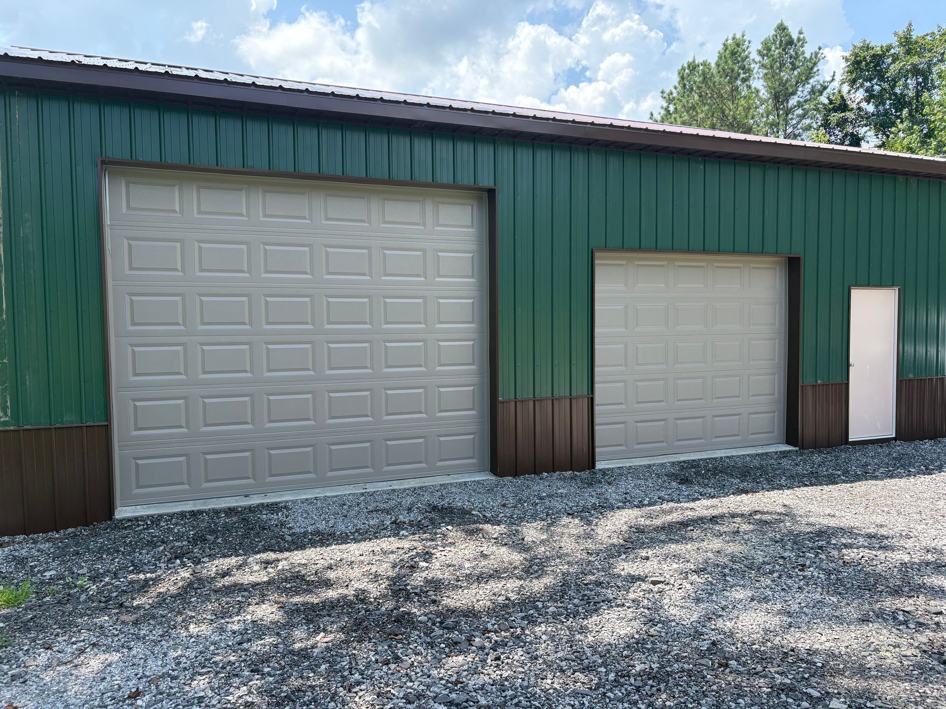 Green and brown metal building with two garage doors and a small white door.