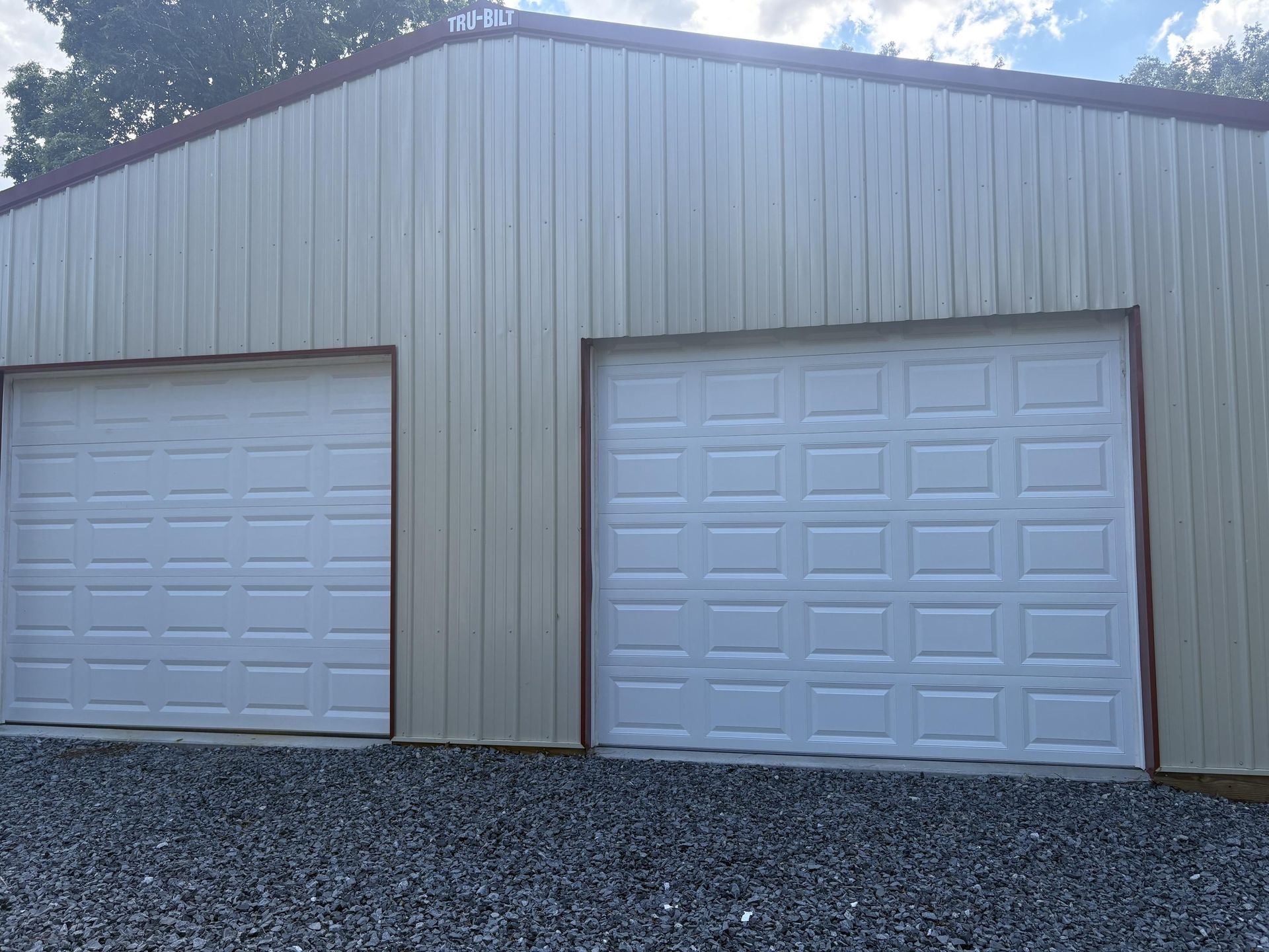 Two white garage doors on a tan metal building with a red trim; gravel in front.