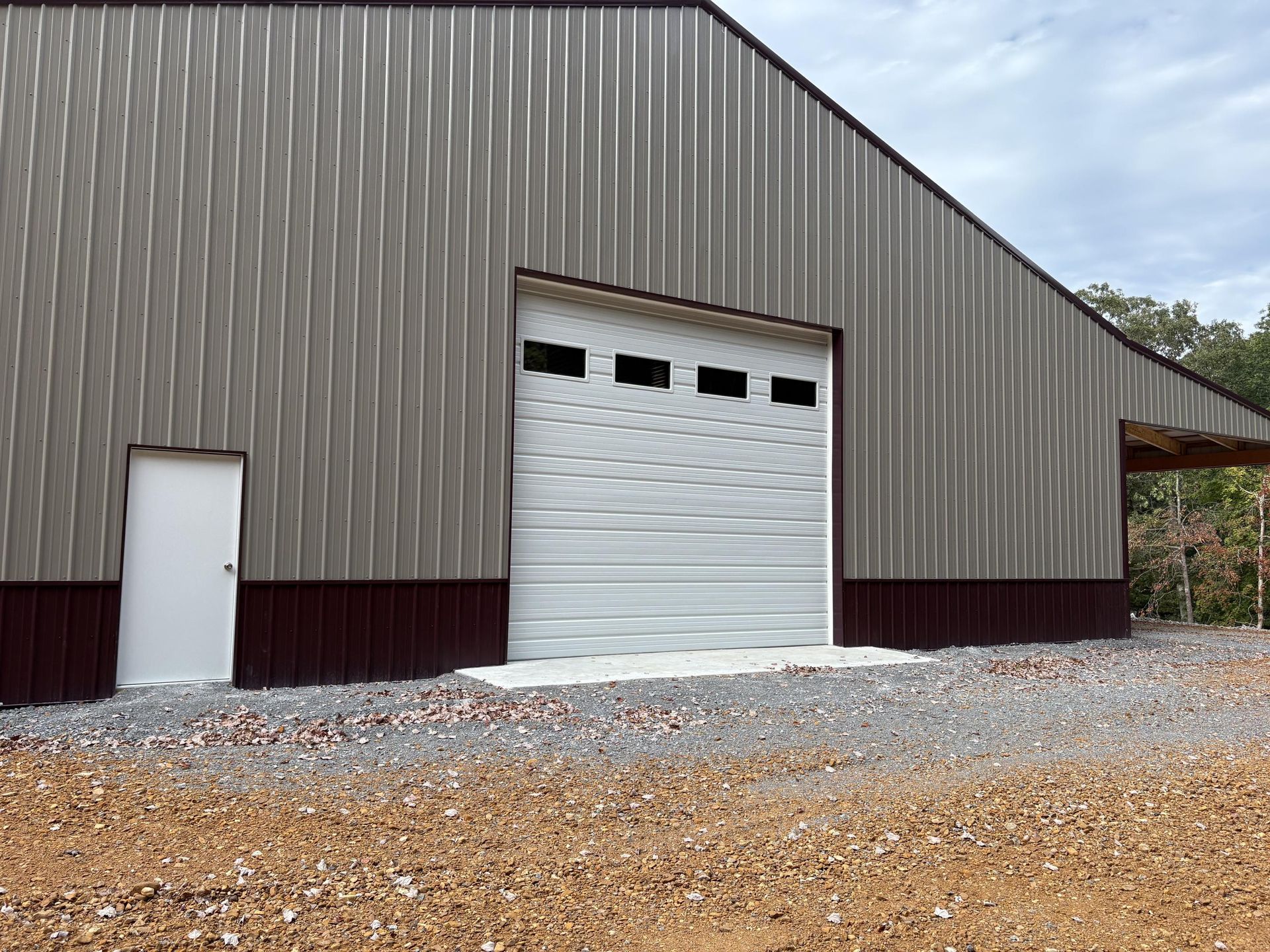 A large metal building with a garage door and a side door; gravel driveway.