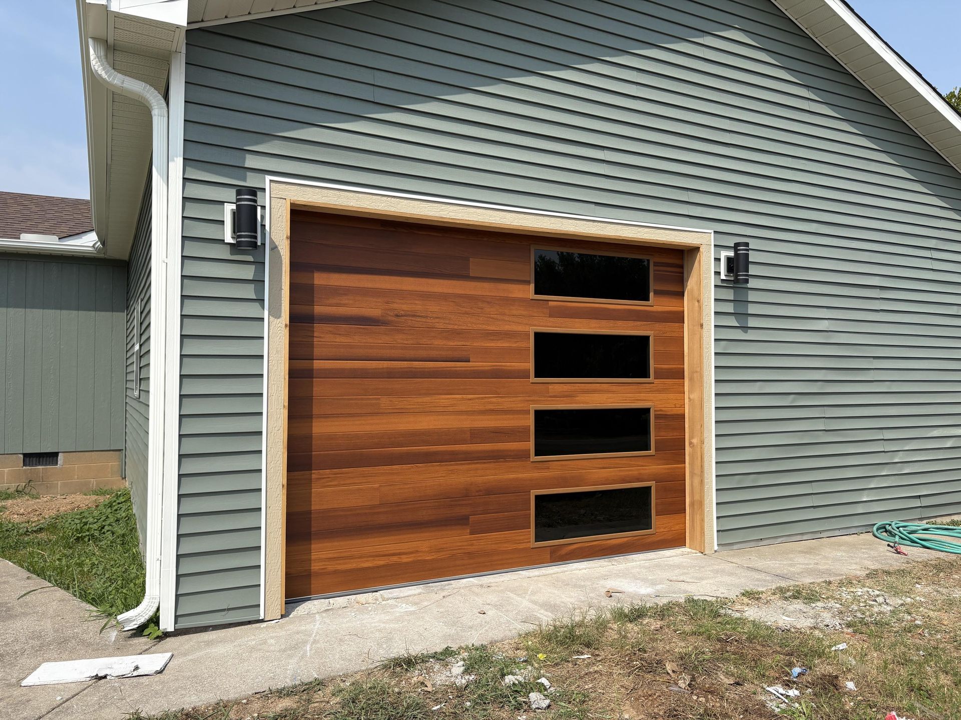 Wooden garage door with windows, on a blue-green house with tan trim and gutter.