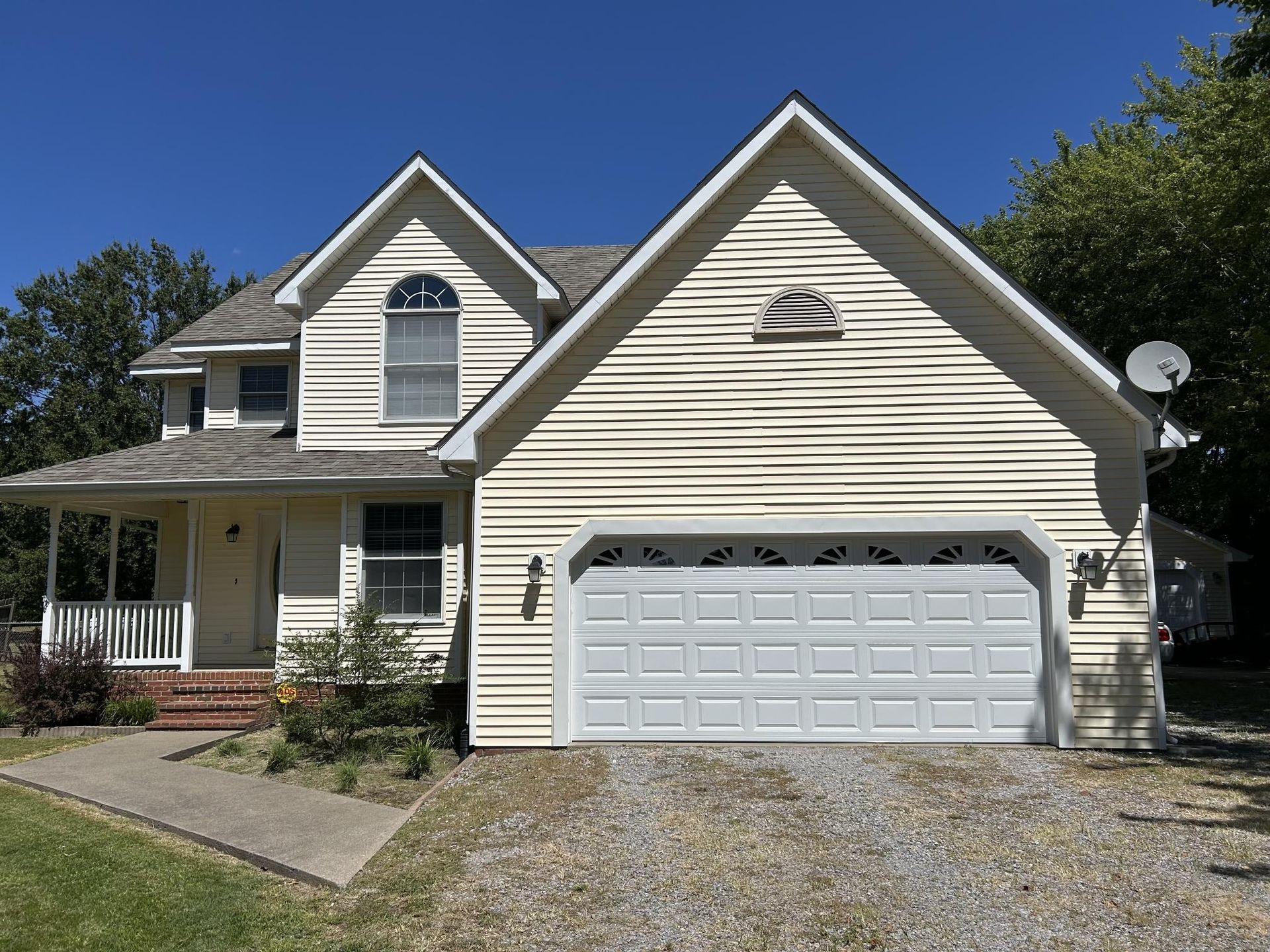 Two-story house with white siding, a gray roof, and a two-car garage under a clear blue sky.