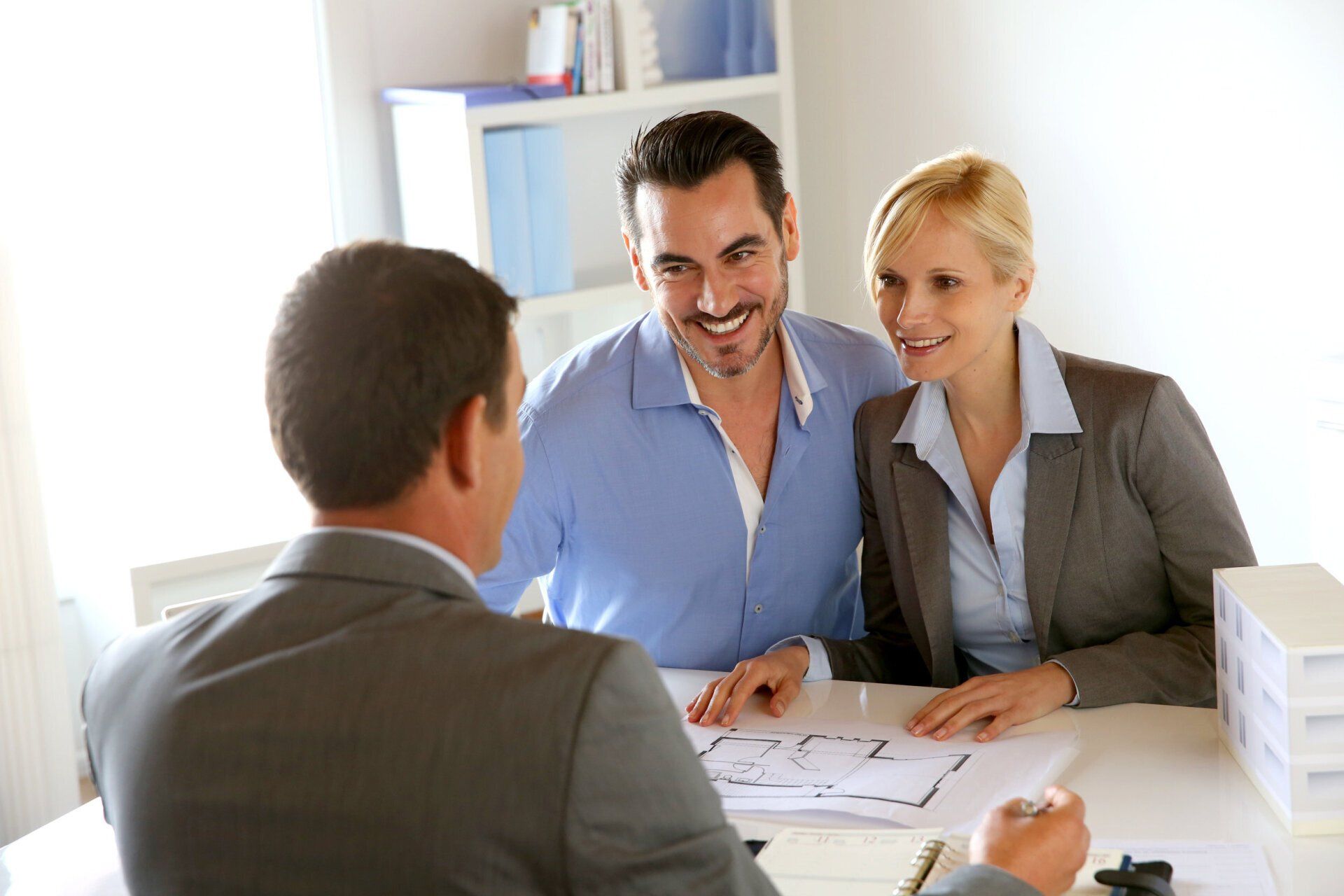 A man and woman are sitting at a table talking to a real estate agent.
