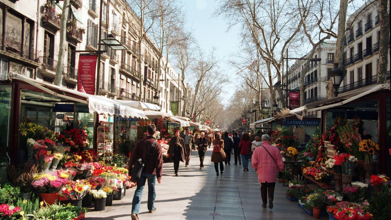Una calle muy transitada llena de flores y gente caminando por ella.