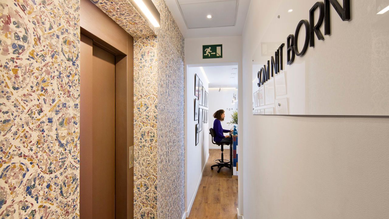 Una mujer está sentada en un escritorio en un pasillo al lado de un ascensor.