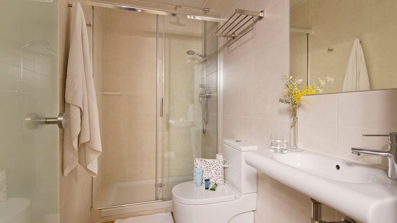 Un baño con inodoro, lavabo, ducha y espejo.