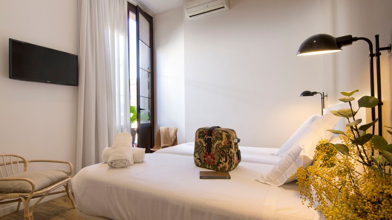 Un dormitorio con dos camas, una lámpara, una televisión y un bolso sobre la cama.