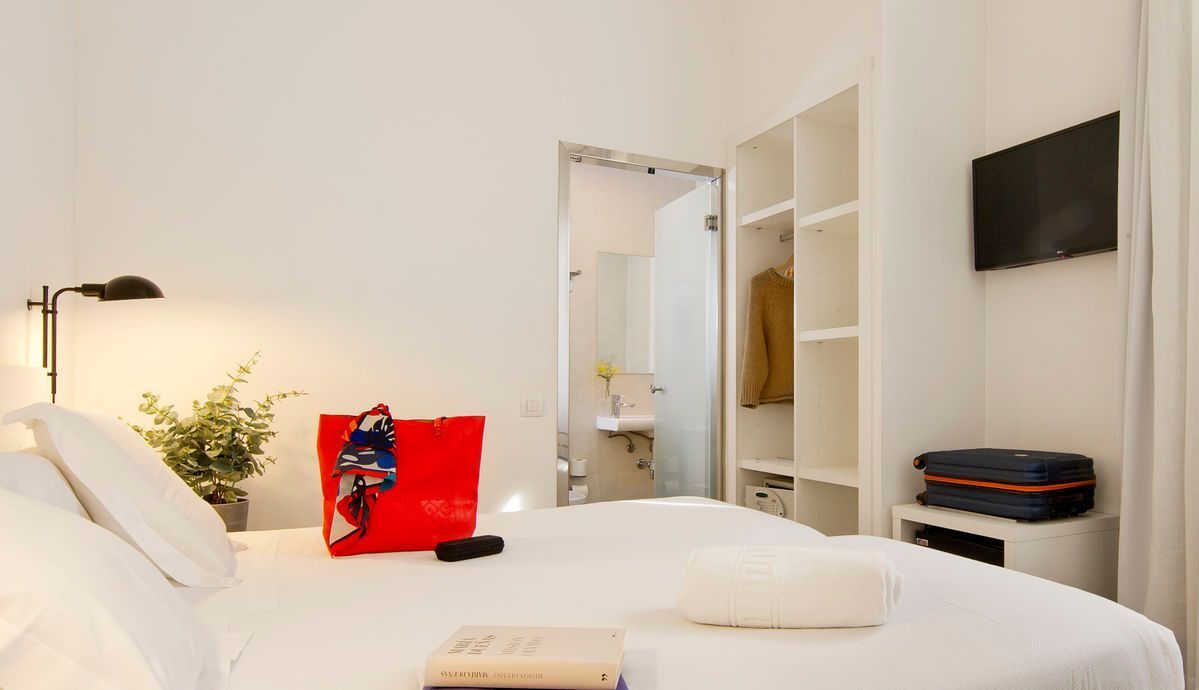 Una habitación de hotel con una cama, televisión y una bolsa sobre la cama.