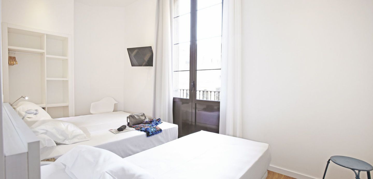 Un dormitorio con dos camas, un taburete y una ventana.