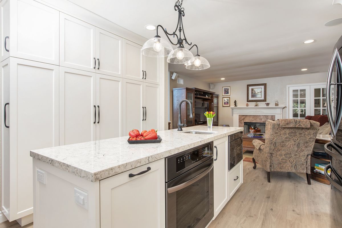 A kitchen with white cabinets , granite counter tops , stainless steel appliances and a large island.
