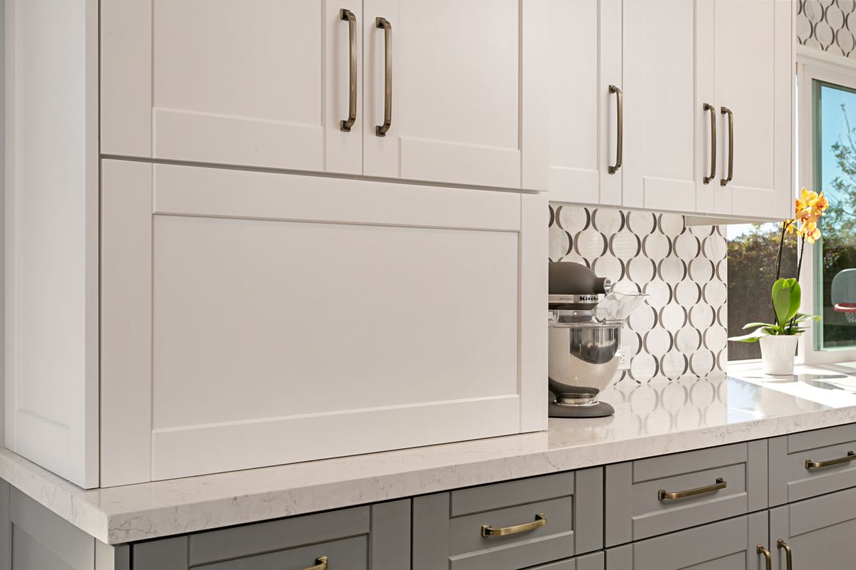A kitchen with white cabinets and gray drawers and a mixer on the counter.