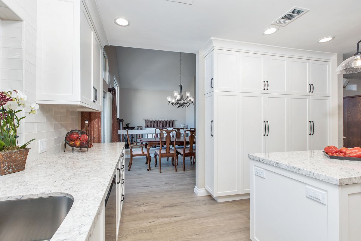 A kitchen with white cabinets , granite counter tops , a sink , and a dining room in the background.