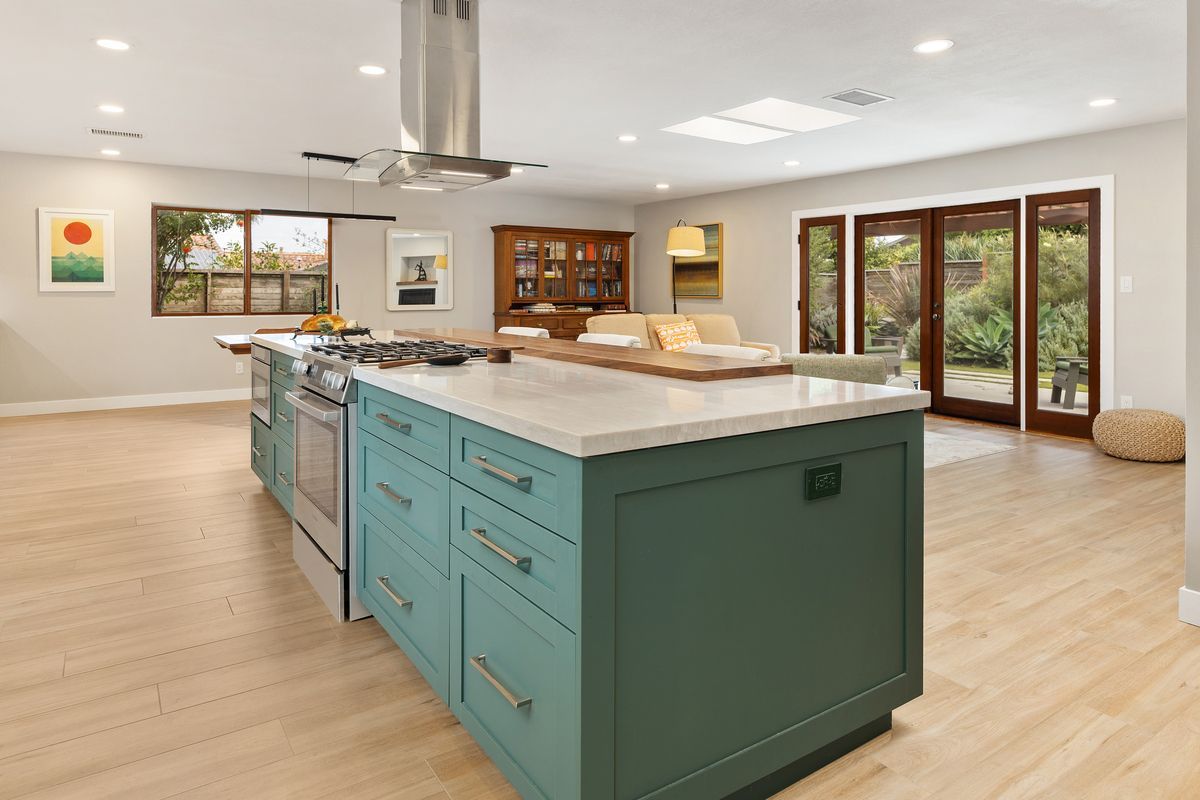 A kitchen with white cabinets , a wooden island , stools and a sink.