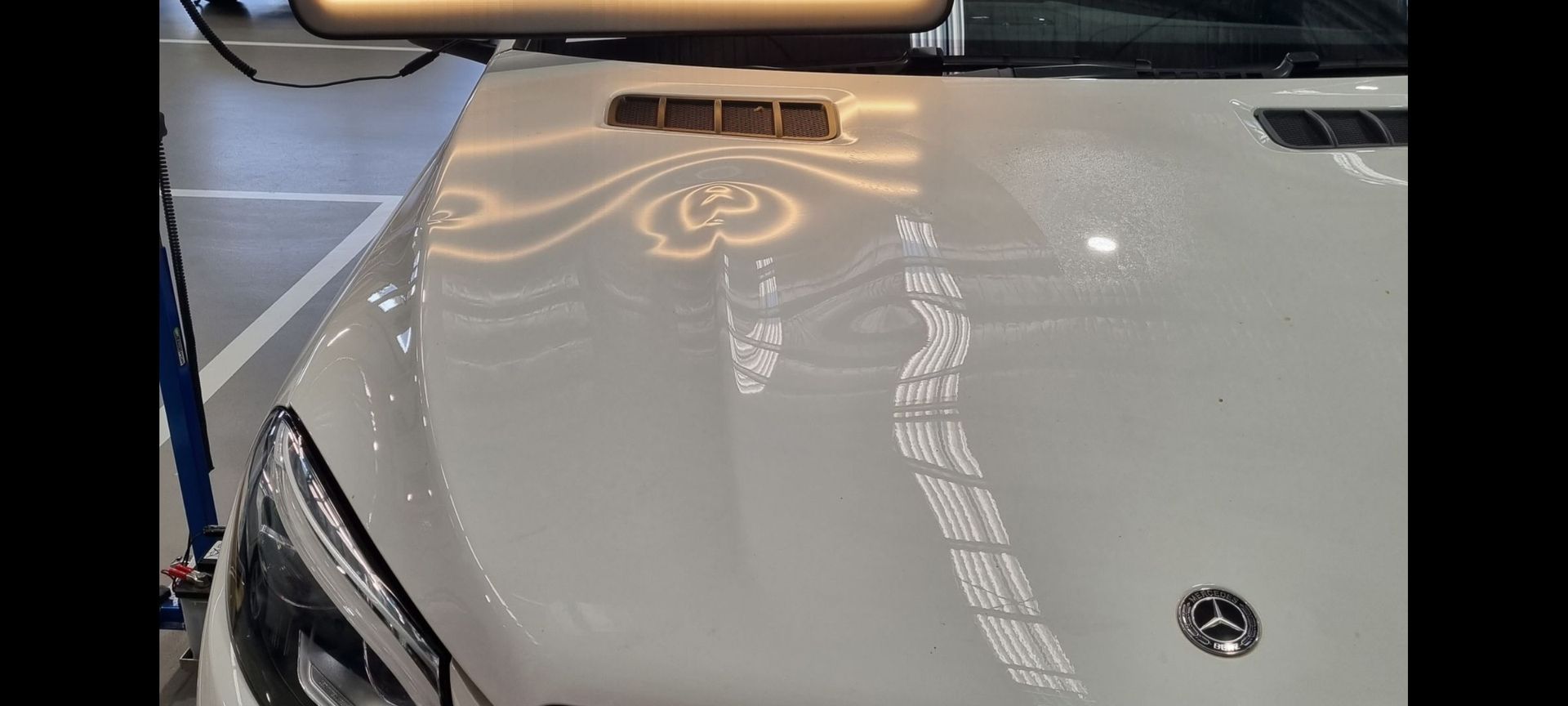 a white mercedes has a dent in the hood-bonnet