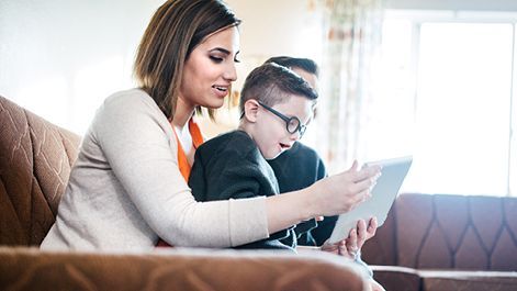 Woman and child look at tablet together, both with surprised expressions; seated on brown couch.
