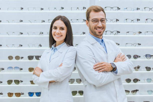 Two opticians in lab coats smiling in front of a glasses display.