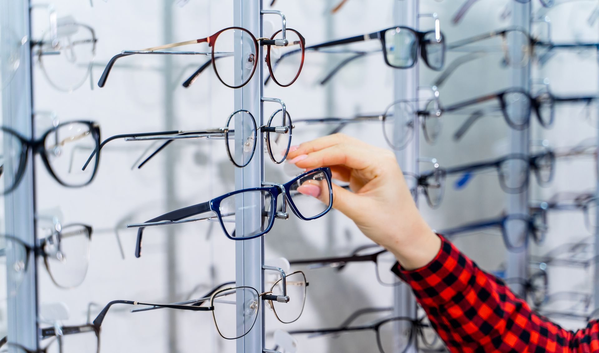 Hand holding blue eyeglasses from a display case filled with various eyewear frames.