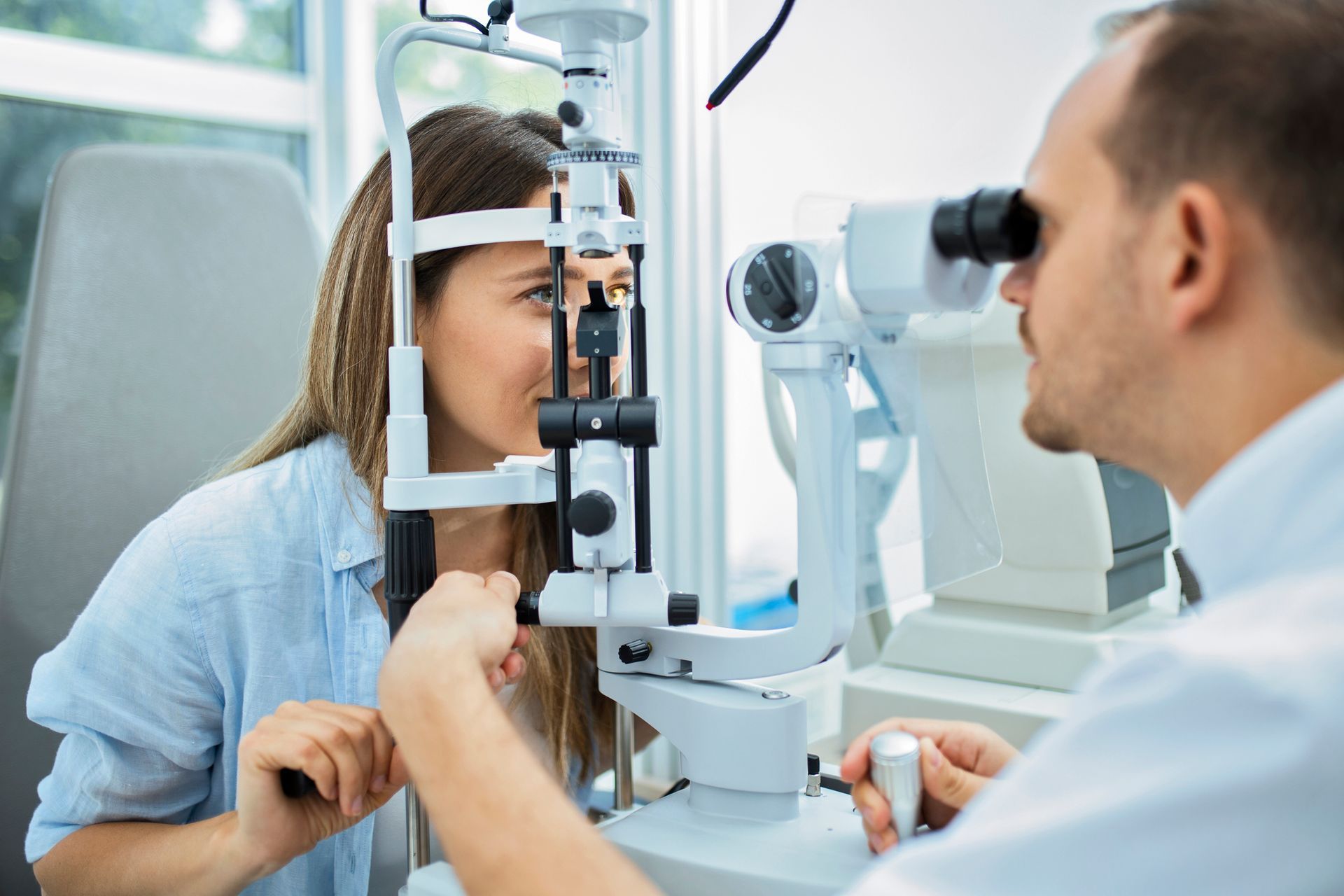 Woman receiving an eye exam from a doctor using a slit lamp. White room, focused faces.