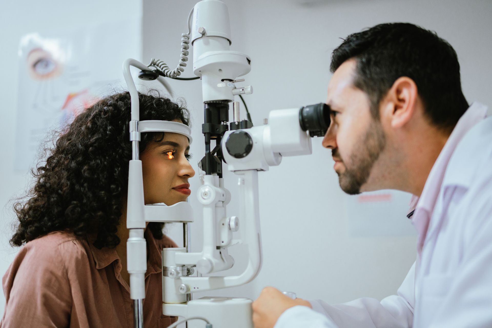 Optometrist examining a person's eye with a slit-lamp microscope in a clinic setting.