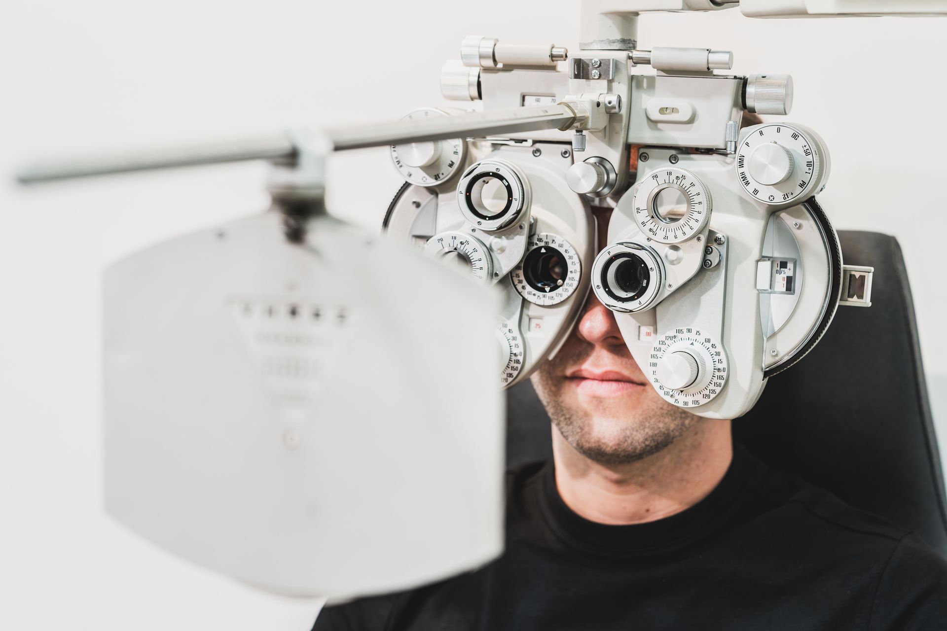 Person having their eyes examined with a phoropter in a white examination room.