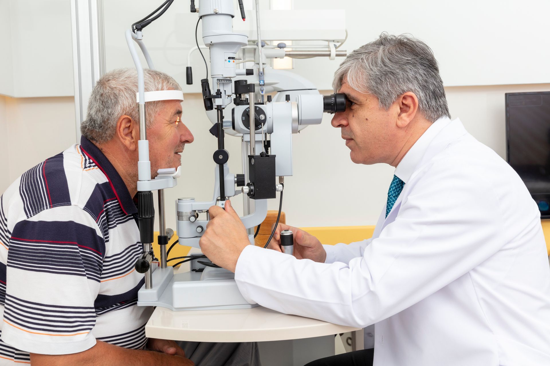 Optometrist examining a patient's eyes with a slit lamp in a doctor's office.