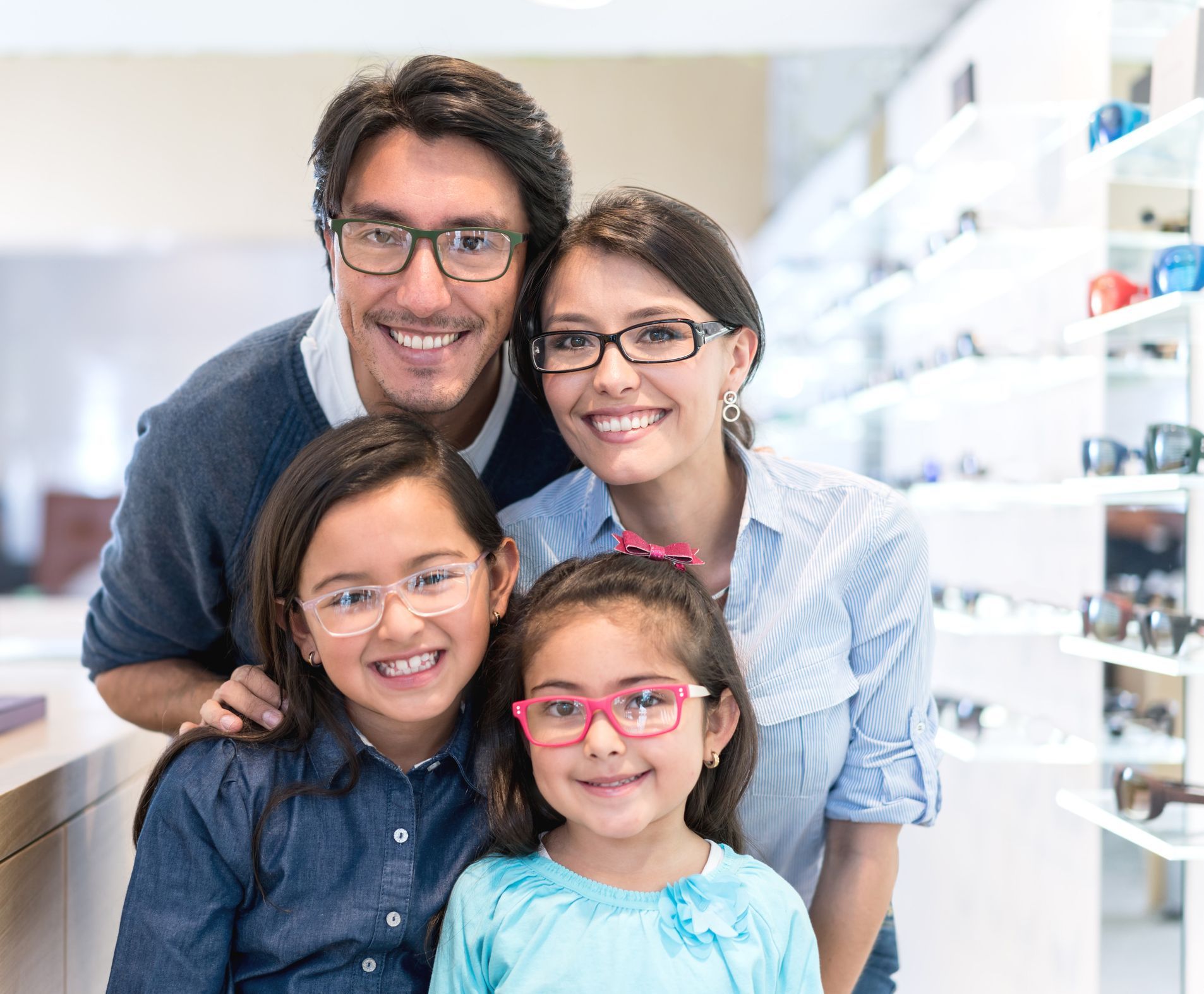 Family with glasses smiling at a store, shelving in the background. Two children in front.