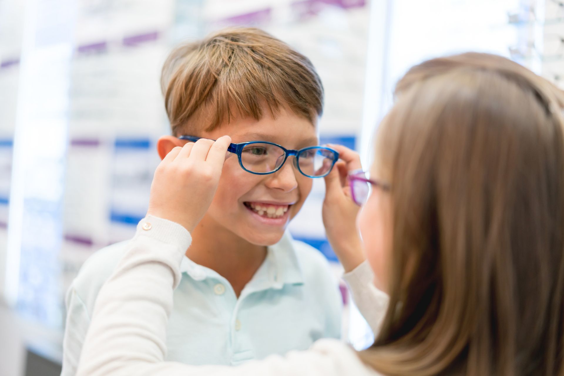 A child smiling as someone adjusts their new eyeglasses in an optician's office.
