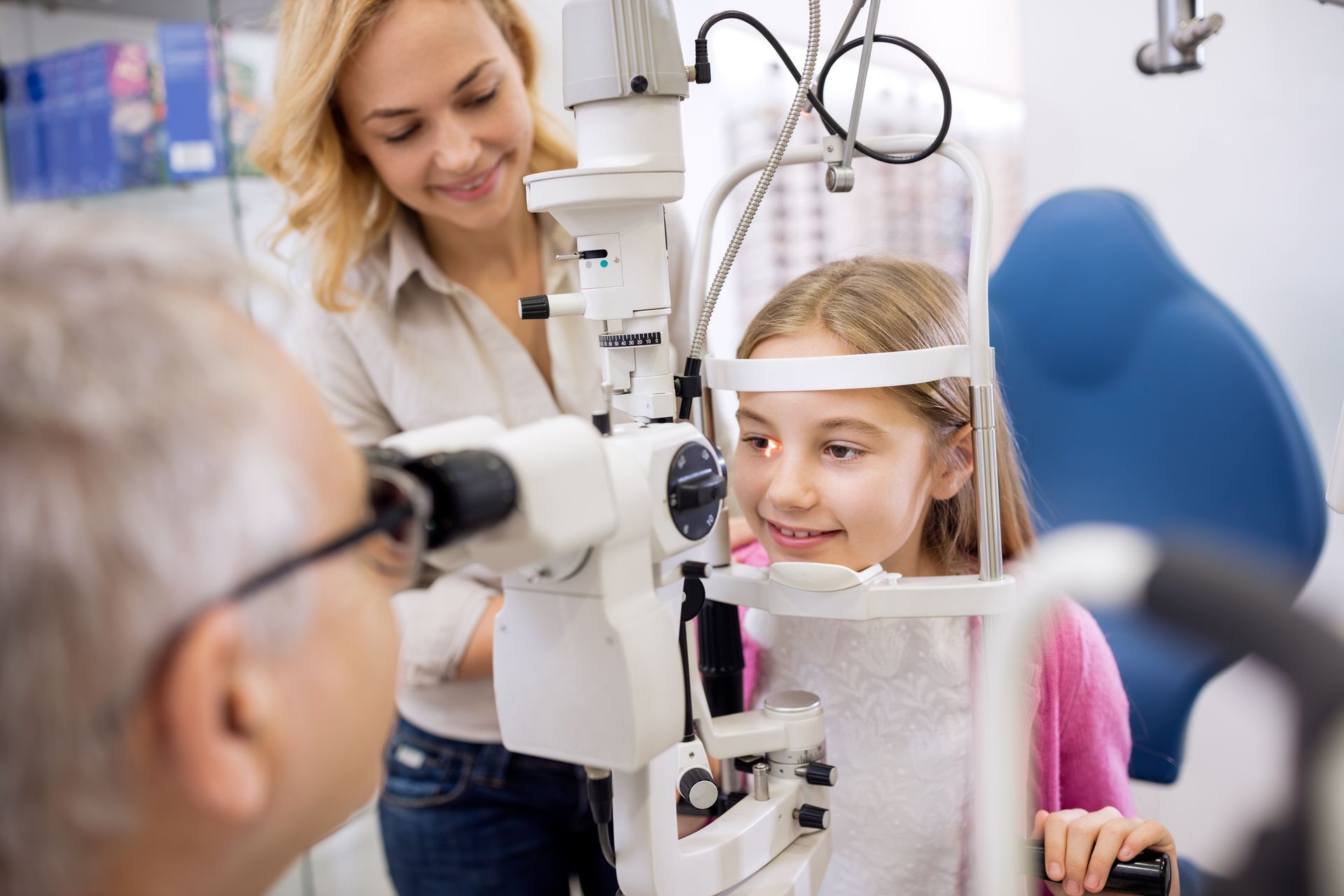 Girl getting an eye exam with an eye doctor, mother watches. Clinic setting.