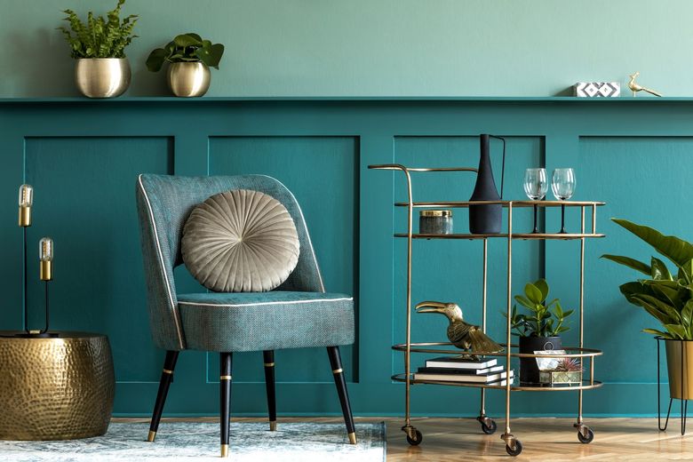 Teal wall with decorative chair and gold bar cart, plants, decor.