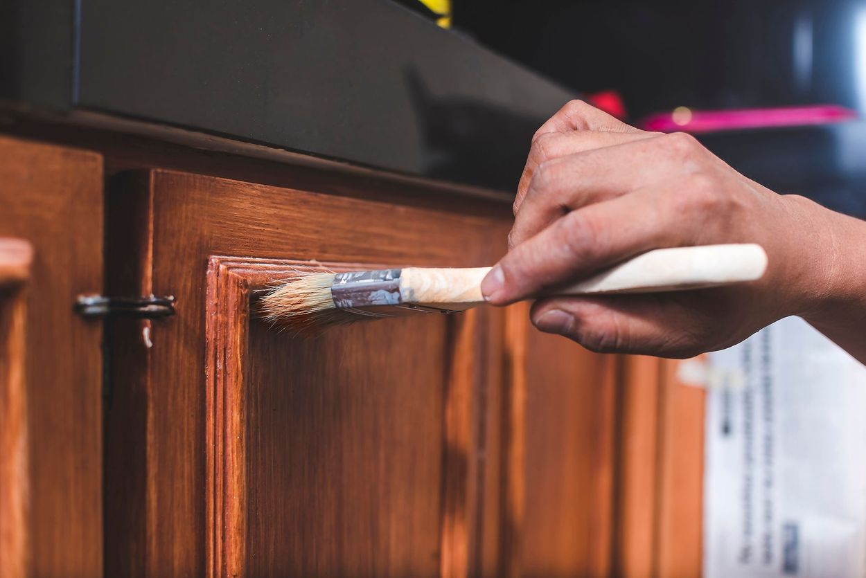 Hand painting a wooden cabinet door with a brush, close-up view.