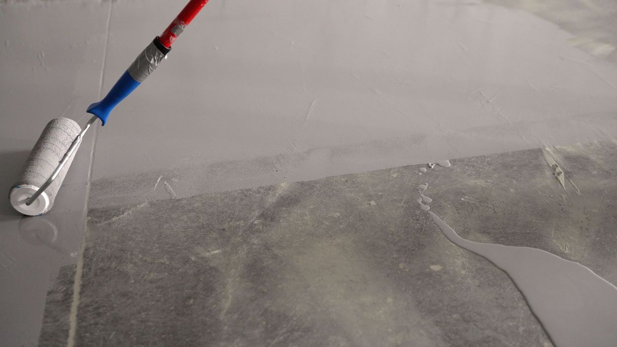 A person using a paint roller to apply gray paint to a surface.