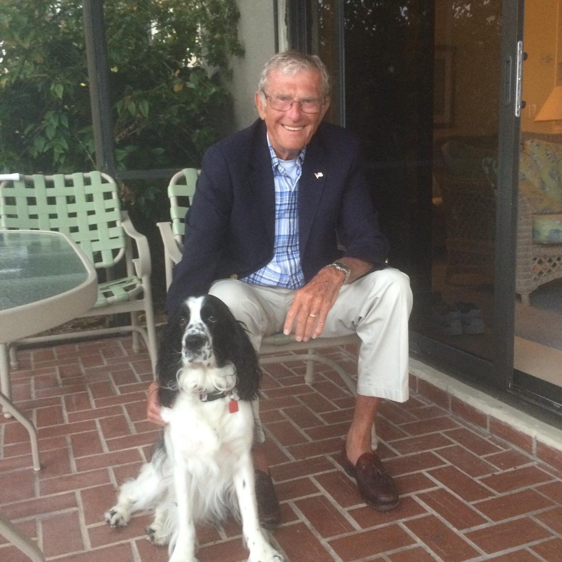 Man in blue blazer and dog on a brick patio, smiling.