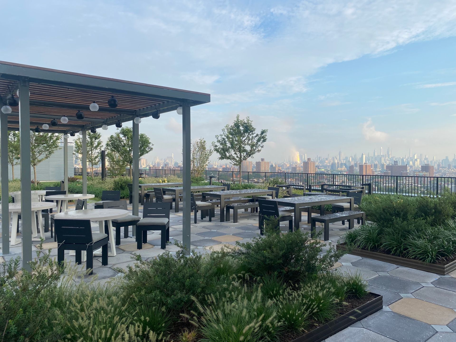 Rooftop patio with tables, chairs, and a city skyline in the distance on a cloudy day.