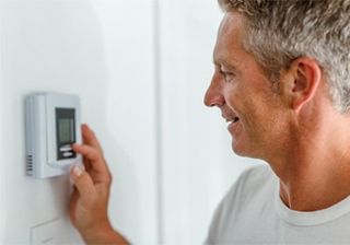 About — Smiling Man Adjusting Thermostat on Home Heating System in Andover, NJ