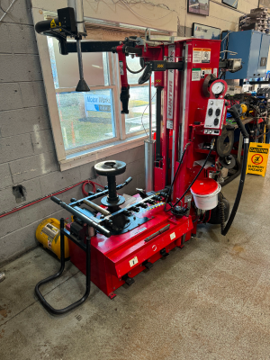 A red tire changer is in a garage next to a window