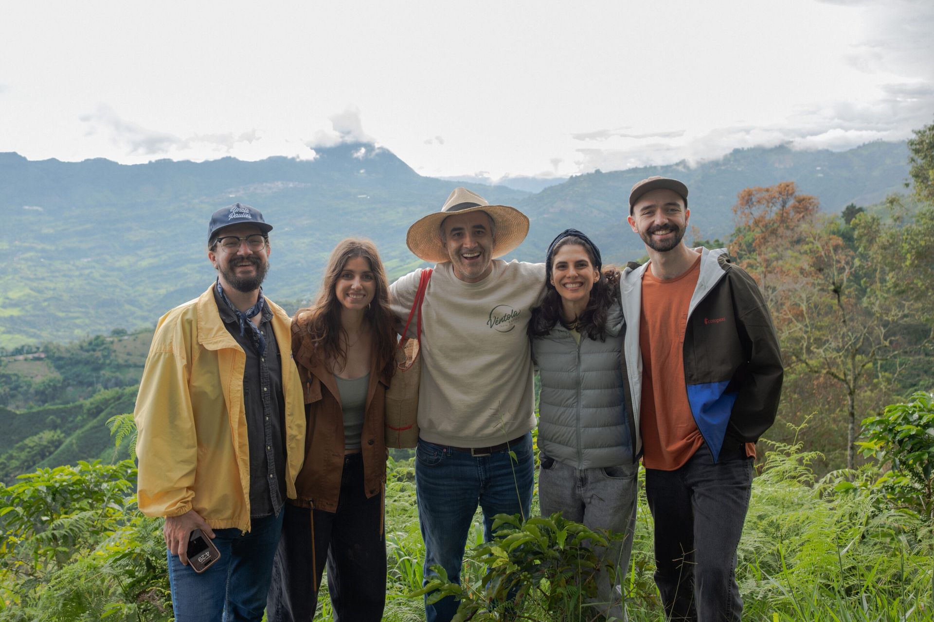 Cinco personas posan sonriendo, fondo de montañas y cielo nublado.