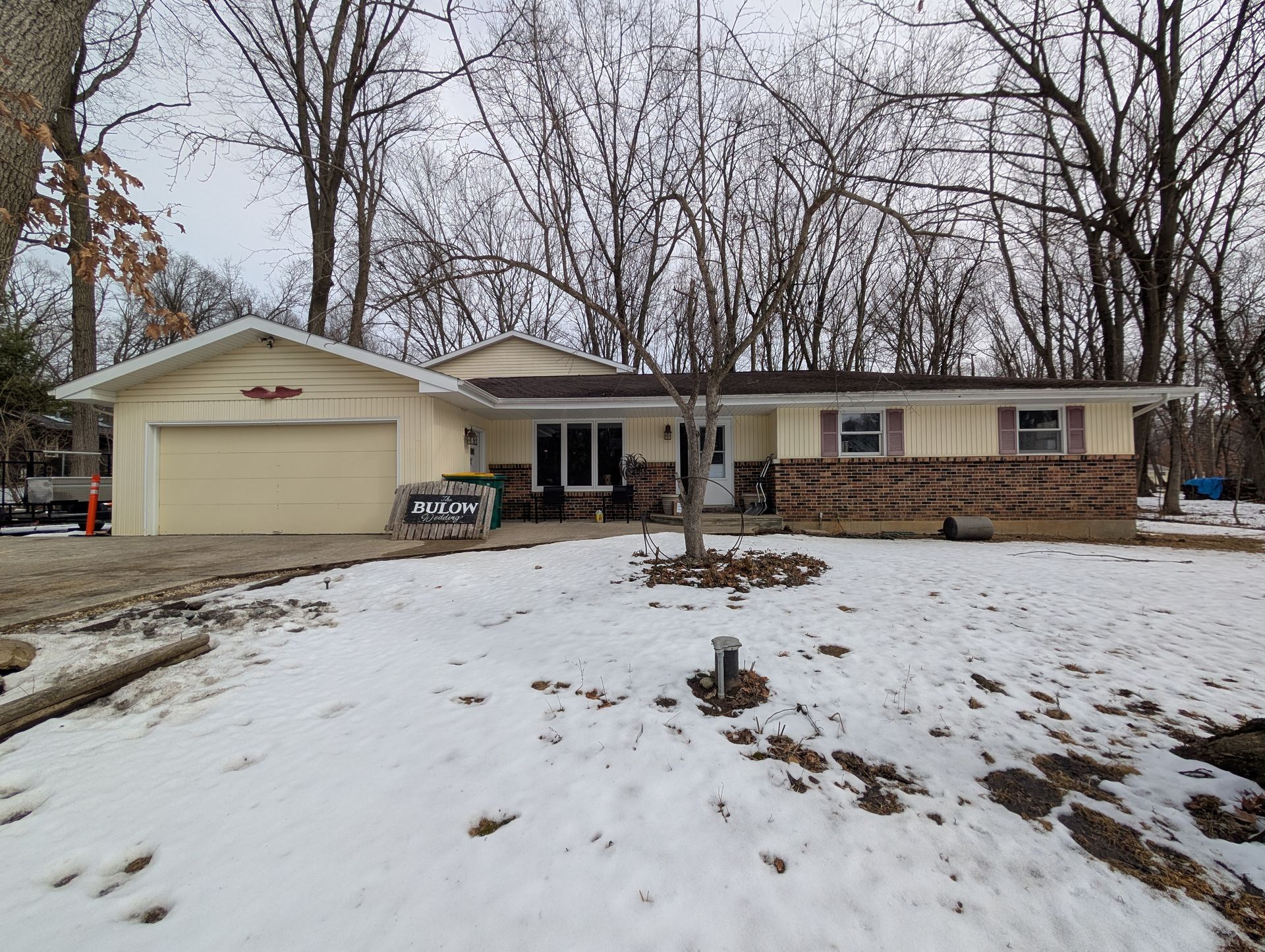 Beige ranch house with snow-covered yard and bare trees; overcast sky.