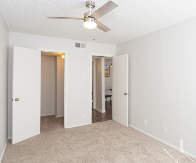 An empty bedroom with a ceiling fan and two doors