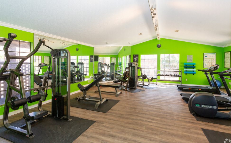 A large gym filled with lots of exercise equipment and green walls.