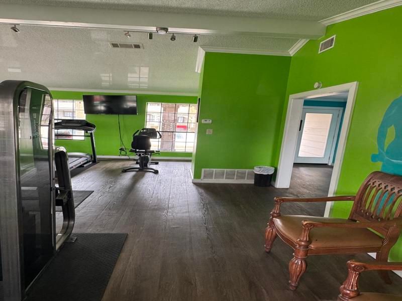 A gym with green walls , a treadmill , a chair and a television.