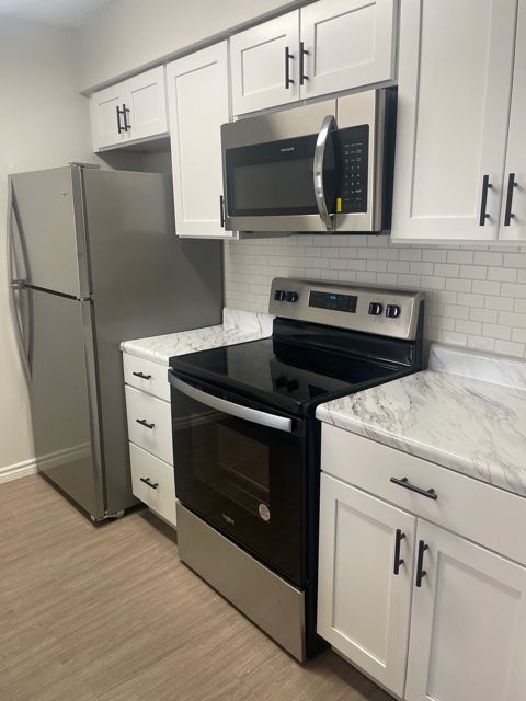 A kitchen with a stove , microwave , refrigerator and white cabinets.