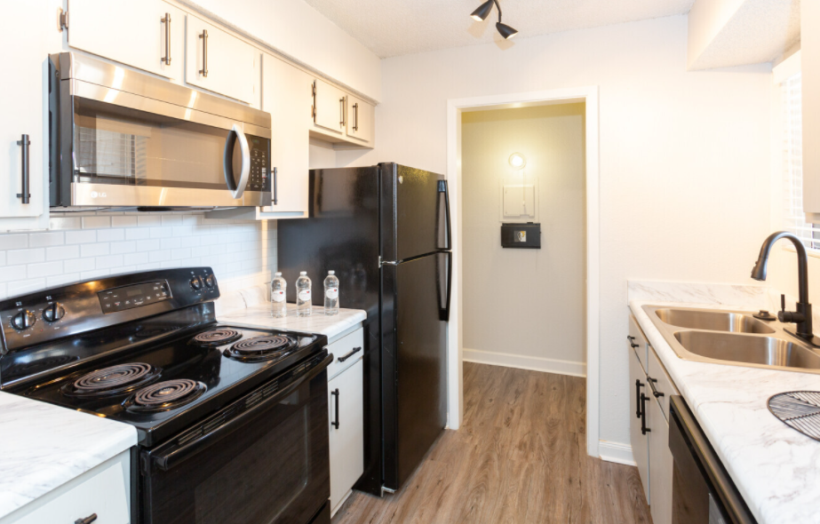 A kitchen with a stove , refrigerator , microwave and sink.